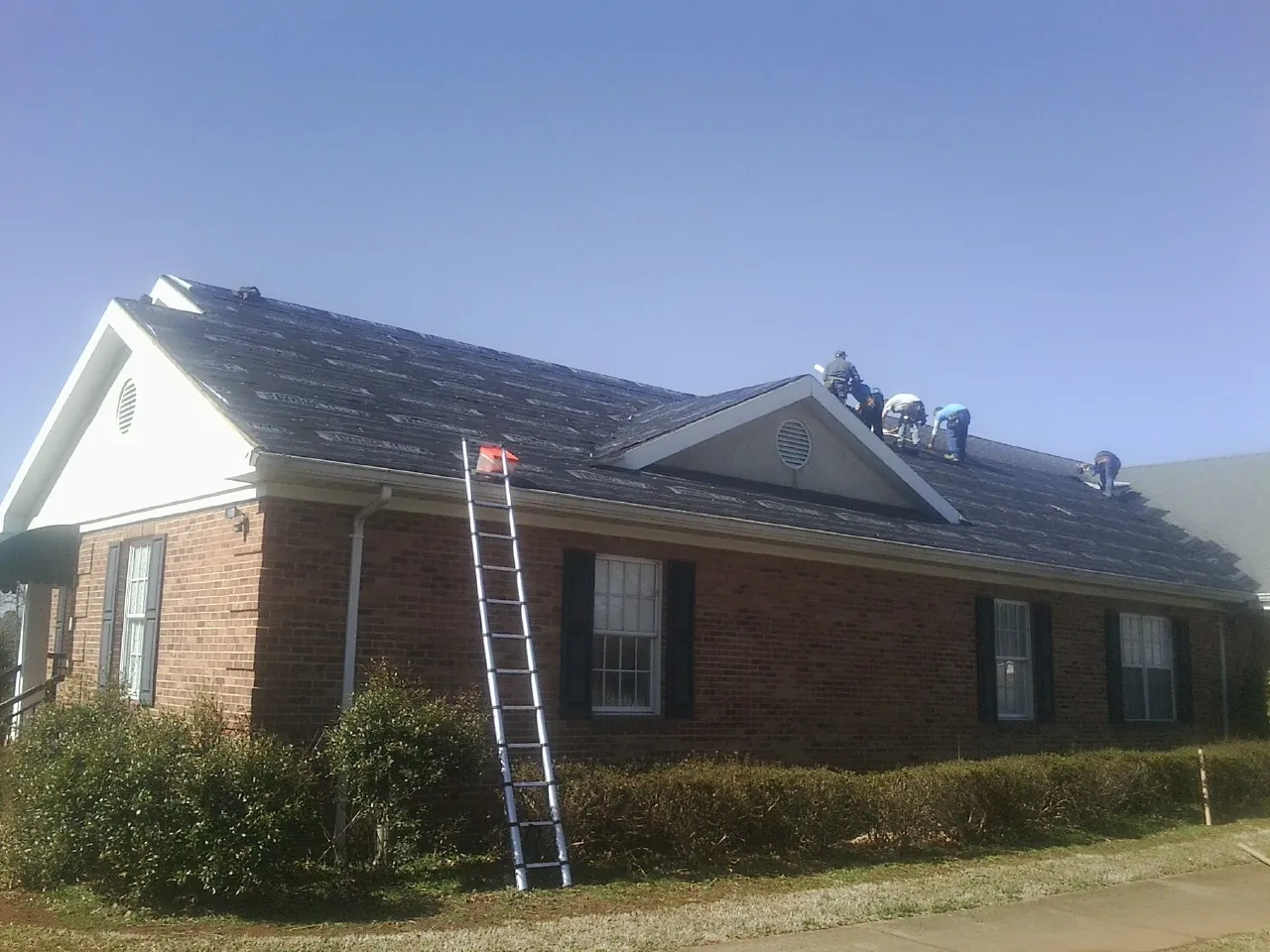 Crew tearing shingles off a brick ranch roof with a ladder set — Emergency Roof Repair work by our crew in Fountain