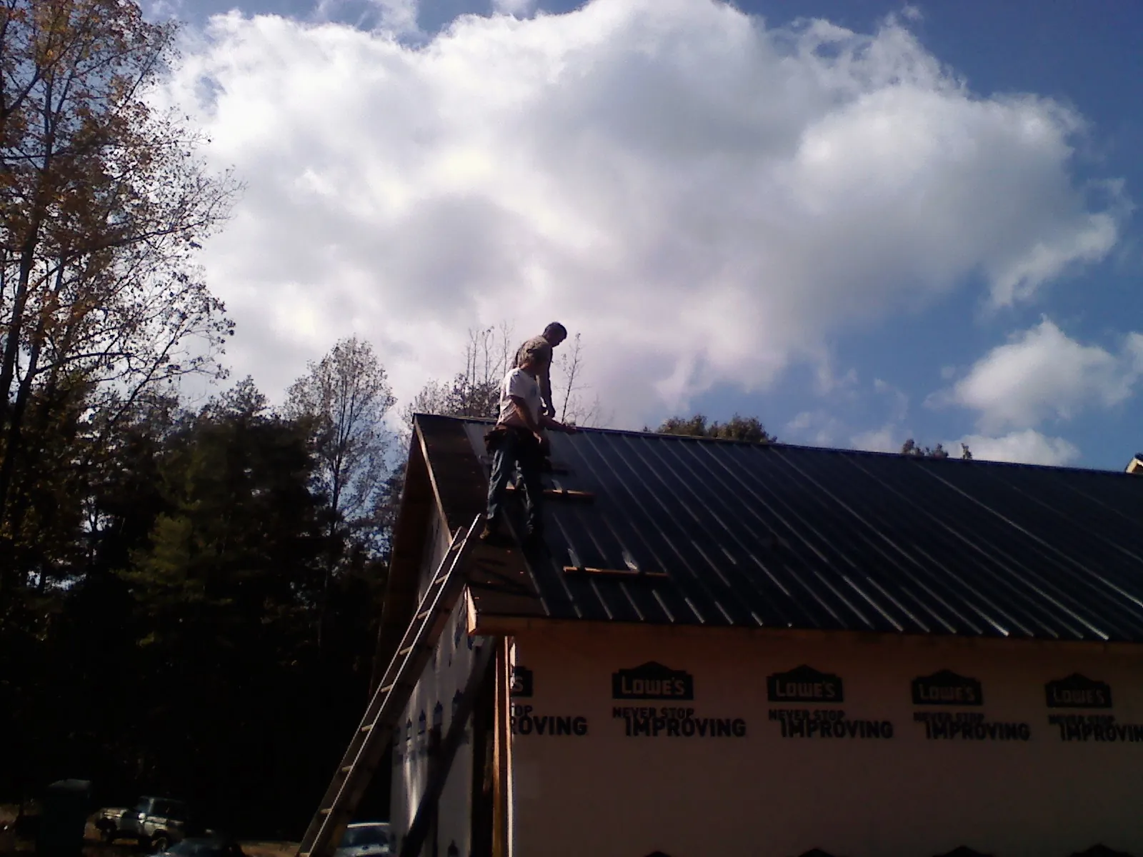 Roofer fastening dark metal panels high against a cloudy sky, from a Roof Inspection job in Fountain