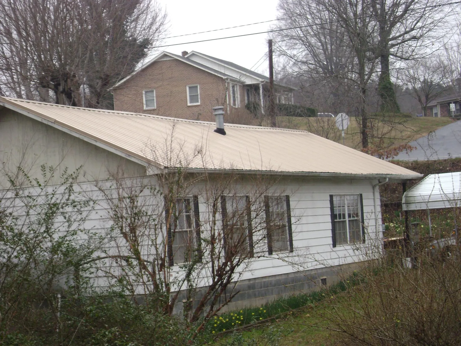 Tan metal roof on a white sided house set into a hillside — Commercial Roofing by Roofing Brothers in Fountain